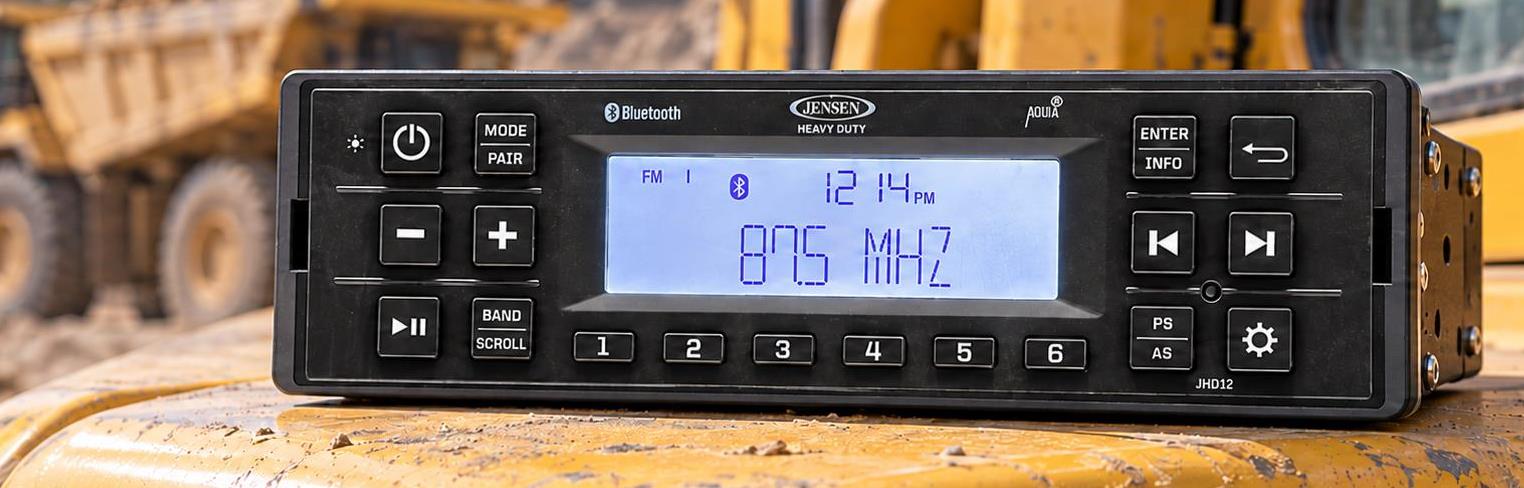 Jensen JHD12 heavy-duty Bluetooth radio shown on a dump truck fender, highlighting its compact short-chassis design for construction equipment.